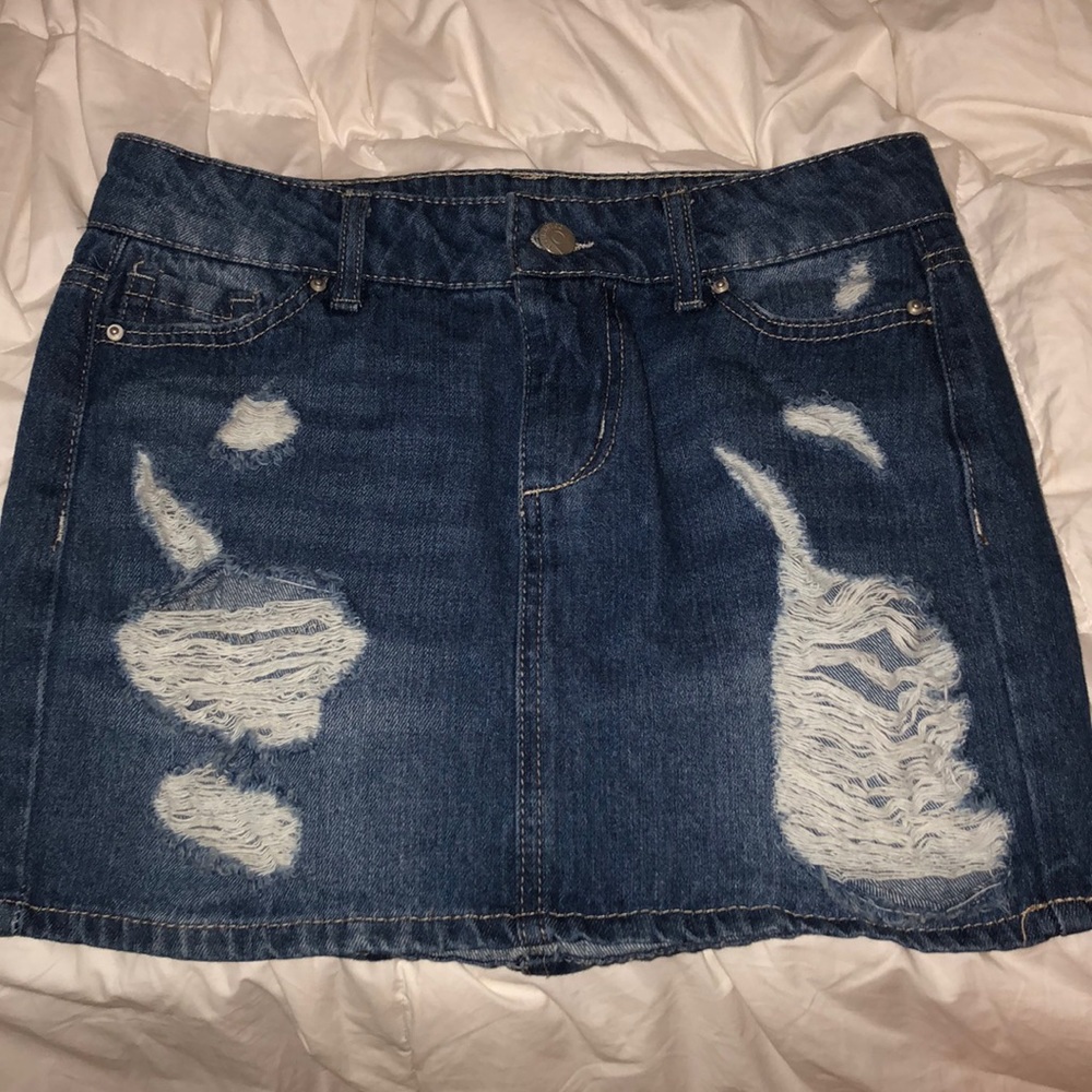 A blue jean skirt with rips on the front.